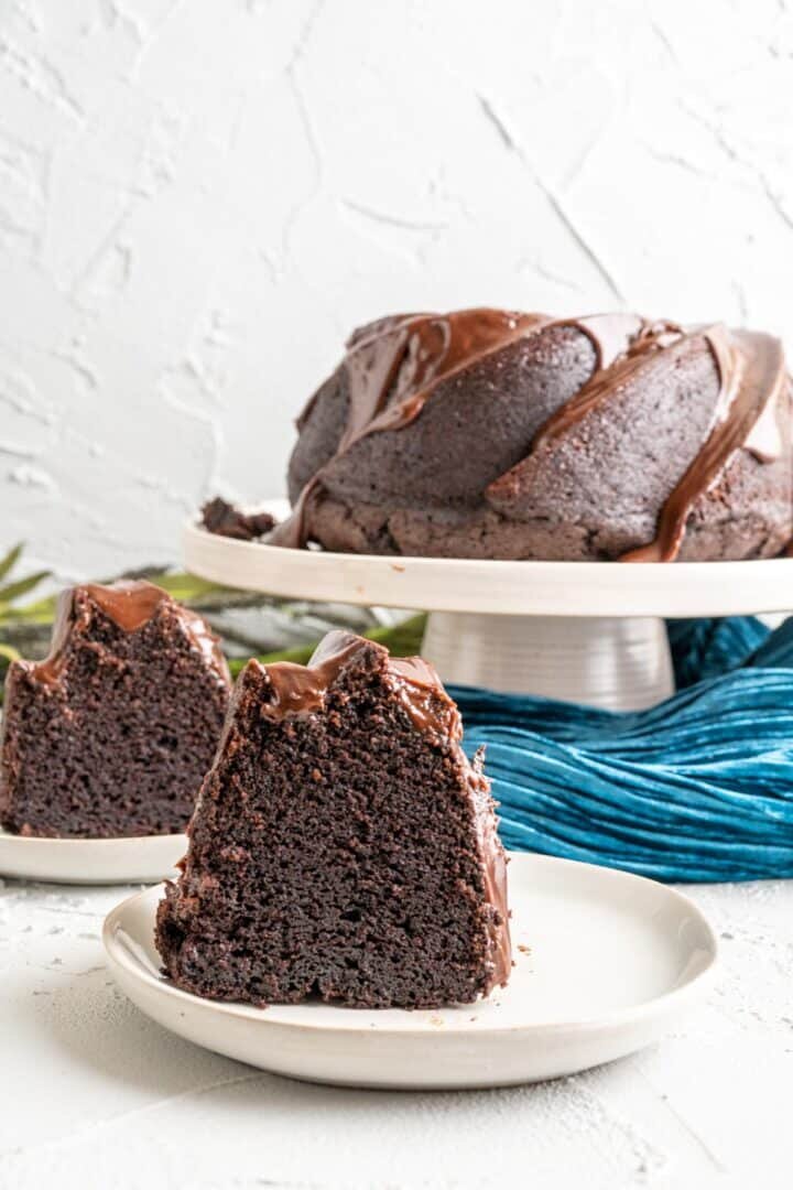 Pieces of chocolate cake on small white plates with the bundt cake in the backdrop.