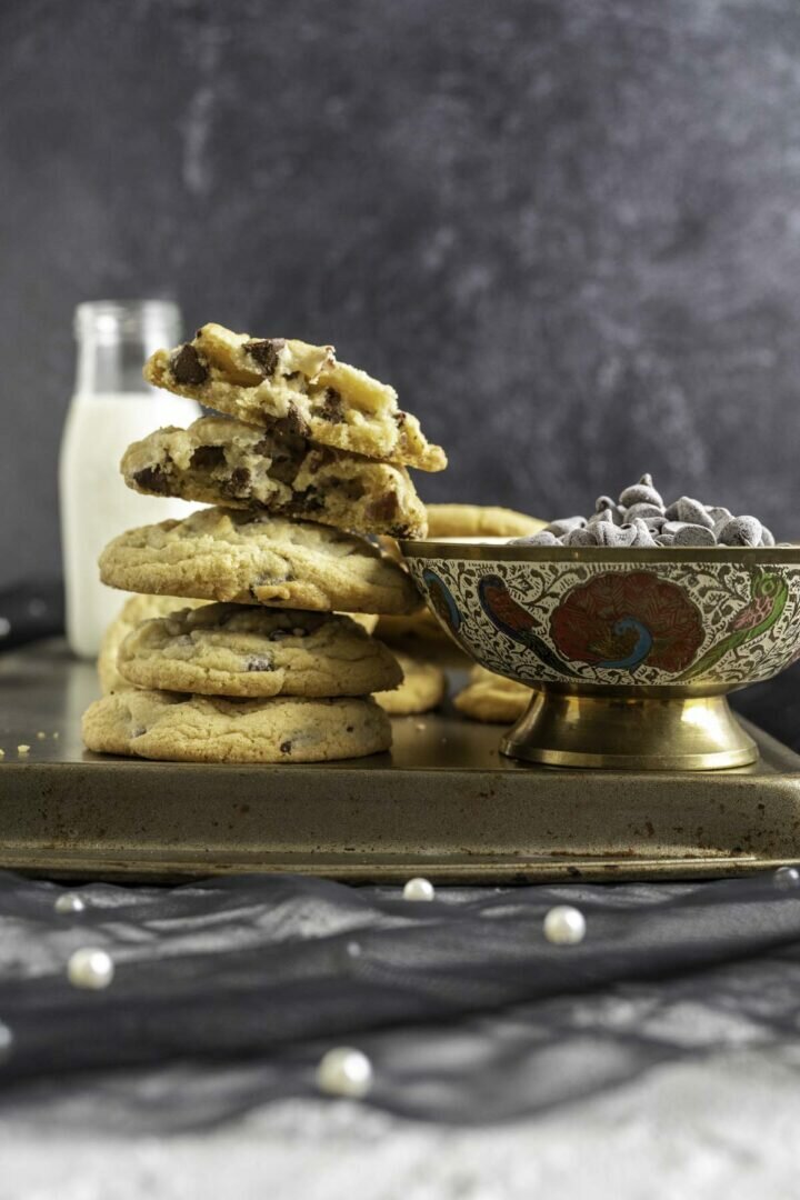 chocolate cookies over each other placed next to a bowl of chocolate chips.