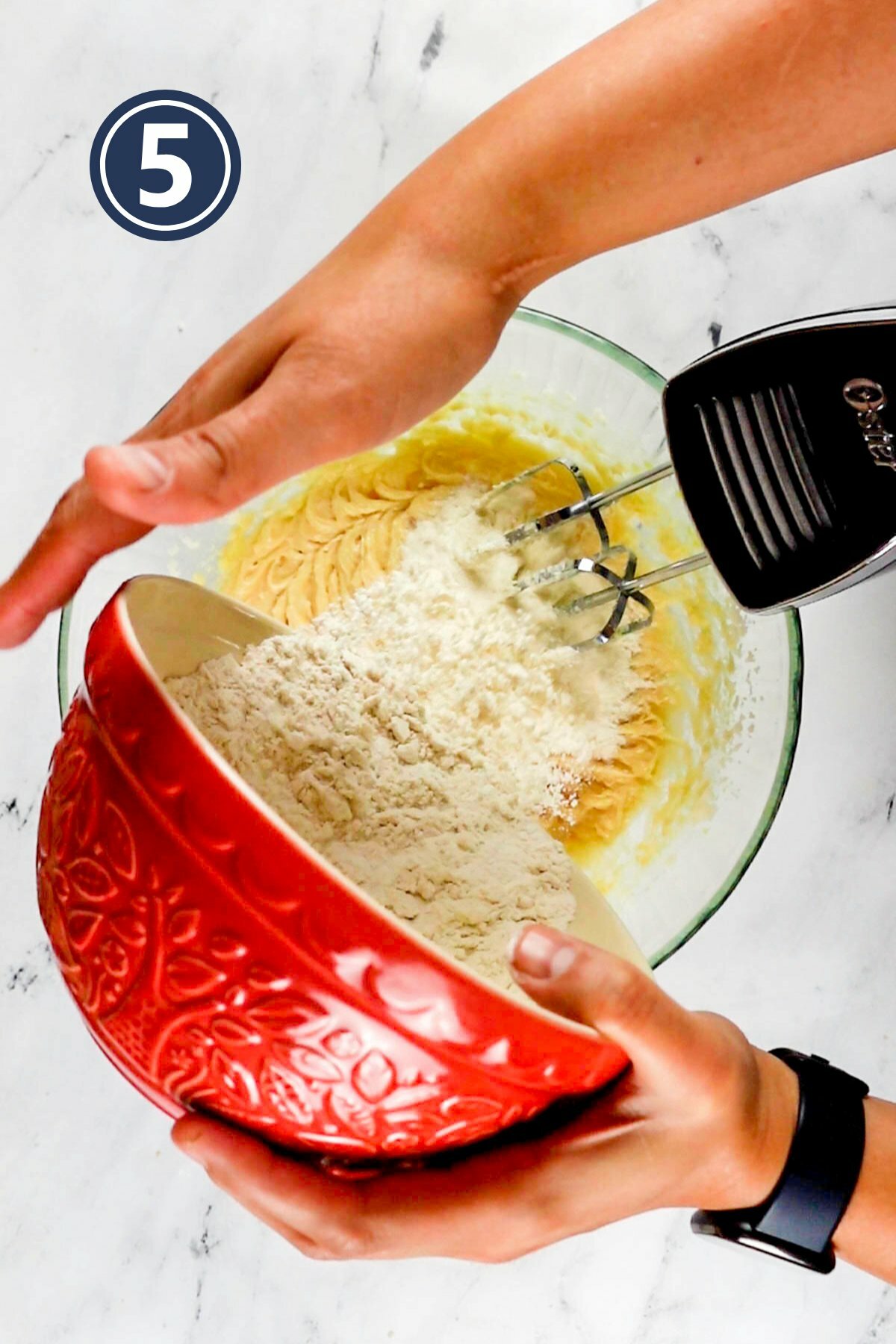 adding the dry ingredients into the wet ingredients in the mixing bowl.